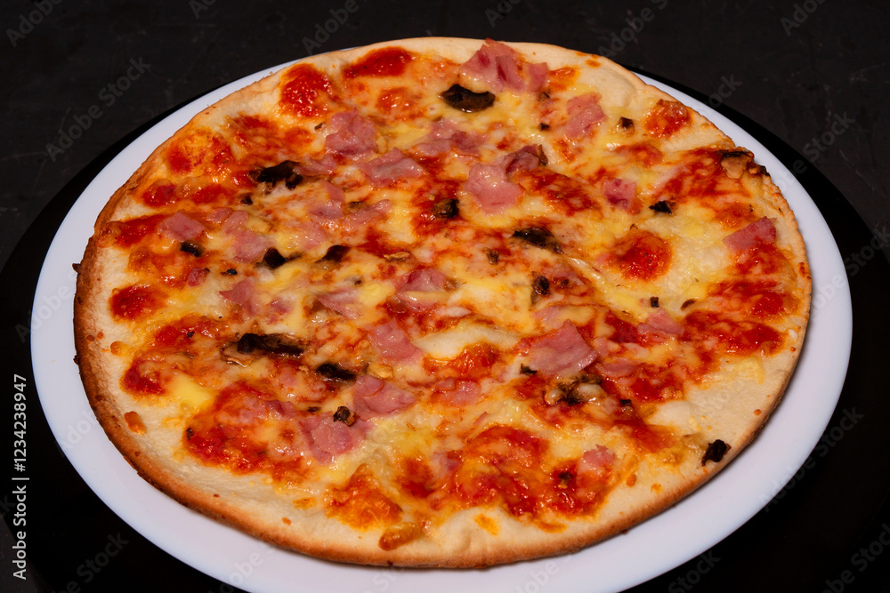 Pizza with ham and mushrooms on a white plate. Black background. Pizza with ham and mushrooms on a white plate. Black background.