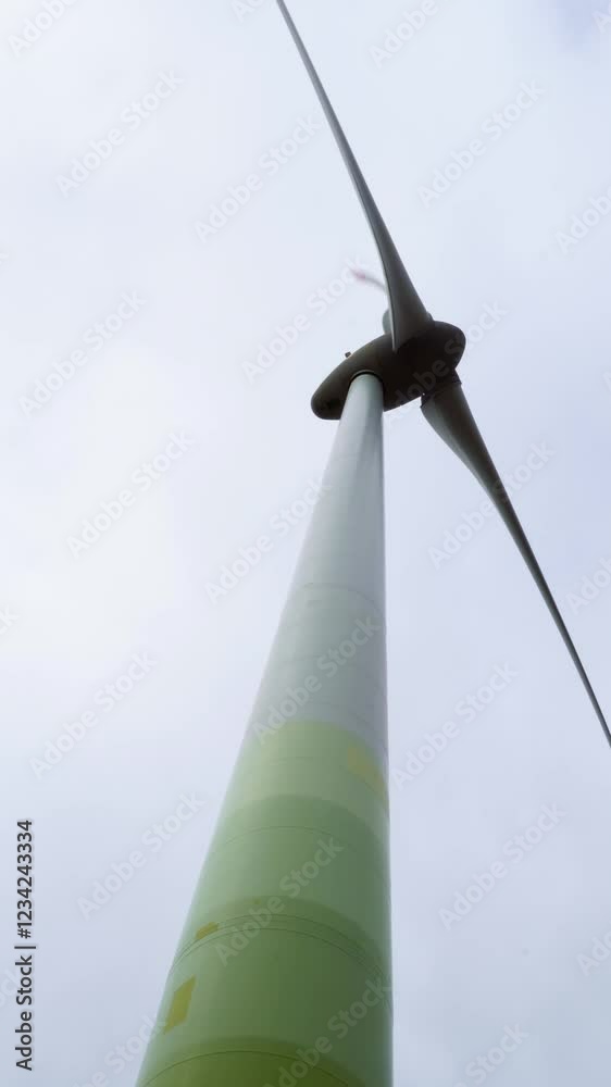 Close-up, low-angle view capturing a green wind turbine generating clean energy against a backdrop of a cloudy sky, emphasizing the importance of renewable energy and sustainability Close-up, low-angle view capturing a green wind turbine generating clean energy against a backdrop of a cloudy sky, emphasizing the importance of renewable energy and sustainability