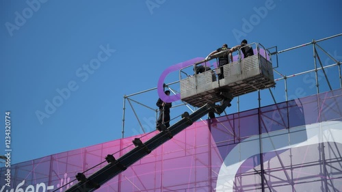  Specialists install street advertising in the cradles of an aerial platform or crane. Professional installers work Installation of a sign on the building. Bottom view