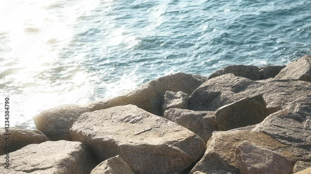 Sunlight reflecting off ocean waves crashing against rugged rocks creates a stunning scene on a bright, sunny day by the shore Sunlight reflecting off ocean waves crashing against rugged rocks creates a stunning scene on a bright, sunny day by the shore