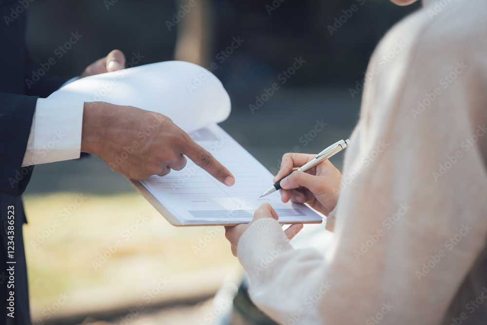 Obraz premium Signing a contract outdoors: A close-up shot showing hands of two people signing a document outdoors. One person is pointing to a specific section of the document. 