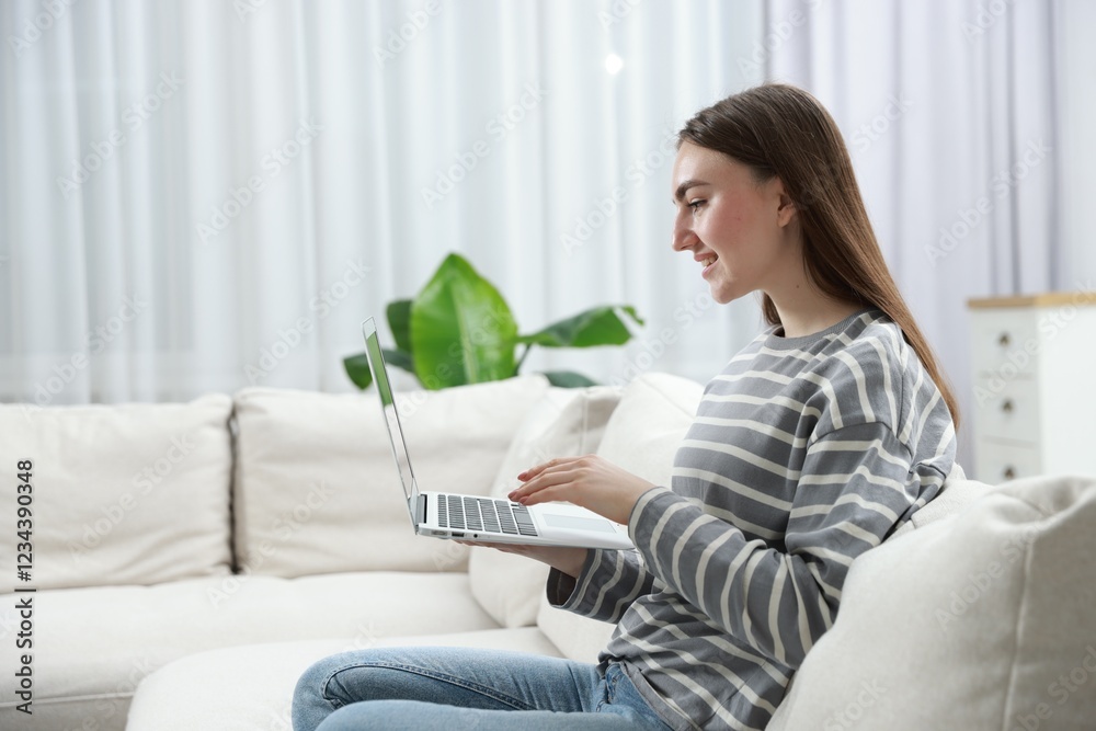 Young woman using laptop on sofa at home. Space for text Young woman using laptop on sofa at home. Space for text