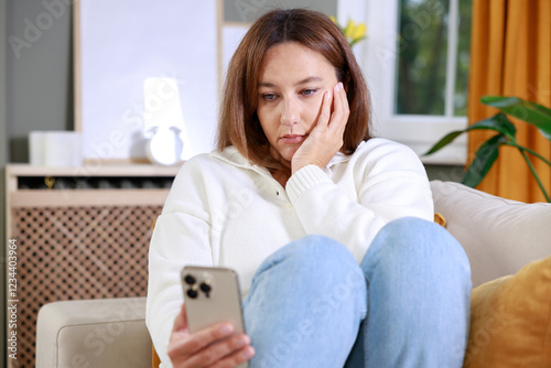 Frustrated young woman with a smartphone in hands while she sitting on the couch at home