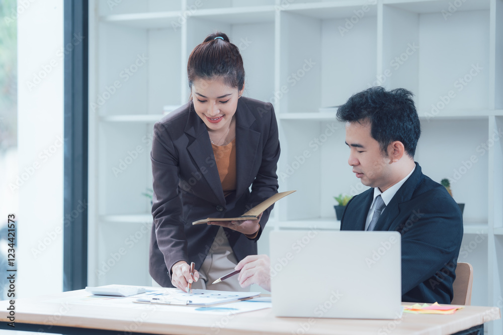 Focused Collaboration: A businesswoman leans in, pointing at a document on the table as she collaborates with her colleague, who is working on a laptop. Focused Collaboration: A businesswoman leans in, pointing at a document on the table as she collaborates with her colleague, who is working on a laptop.