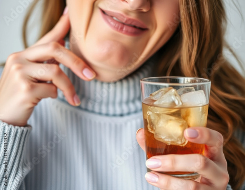 Mujer que sufre de sensibilidad dental sostiene su mandíbula con una mano y con la otra sostiene un vaso con refresco y mucho hielo
