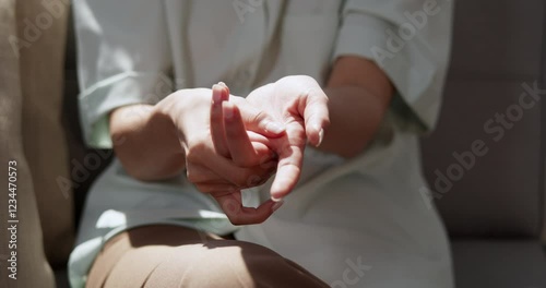 A close-up of an individual massaging her palms using her thumb while sitting on a chair. photo