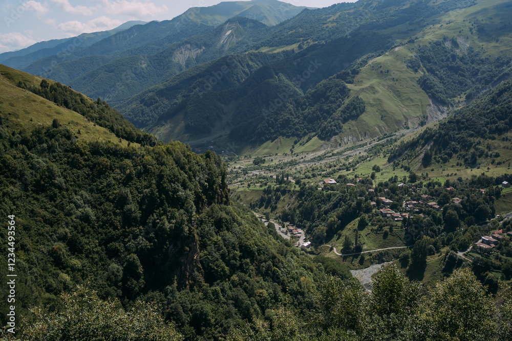 Naklejka premium Scenic mountain valley along the Georgian Military Road. Green hills, a winding river, and a small village in the highlands. Summer landscape in the Caucasus Mountains