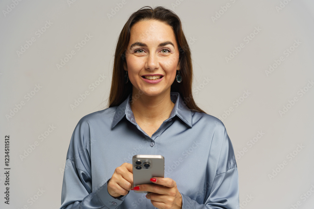 Woman smiling while holding a smartphone in a minimalist indoor setting Woman smiling while holding a smartphone in a minimalist indoor setting