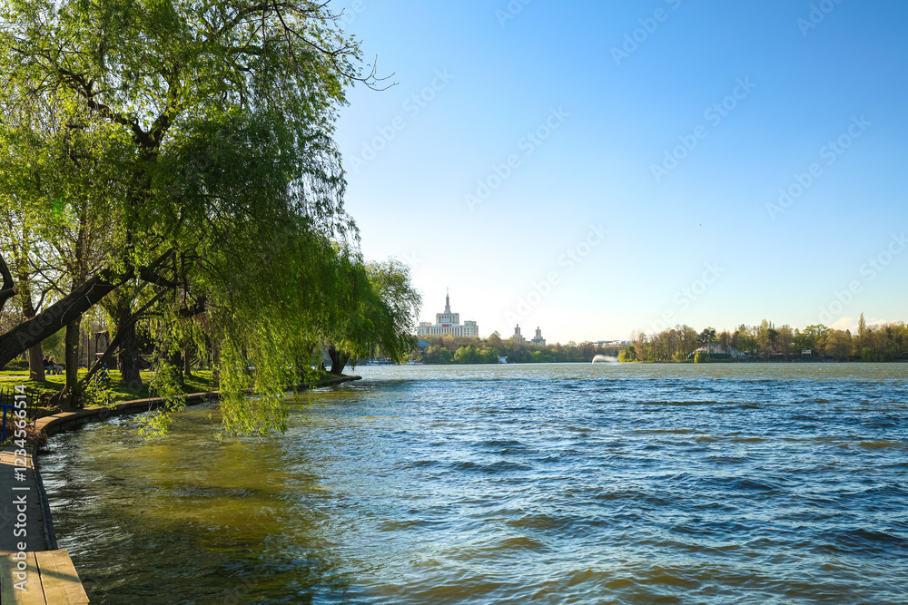 A peaceful park view in Bucharest during springtime, with lush green lawns, blooming trees, and a serene lake reflecting the clear blue sky. An ideal spot for relaxation. Herastrau King Michael I park