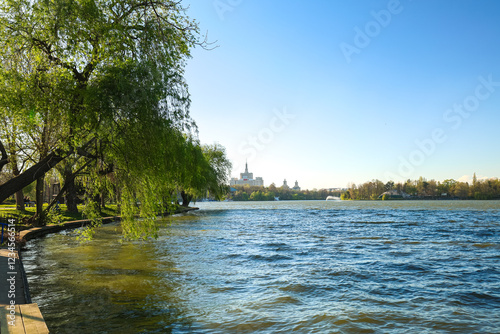 Obraz na płótnie A peaceful park view in Bucharest during springtime, with lush green lawns, blooming trees, and a serene lake reflecting the clear blue sky. An ideal spot for relaxation. Herastrau King Michael I park w salonie