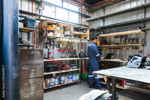Latin mechanic working on laptop in organized workshop with tools and equipment