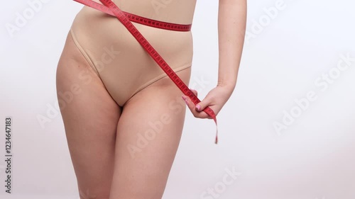 Slender young girl in beige bodysuit measures waist and hips with tape measure. Weight loss and healthy lifestyle concept.