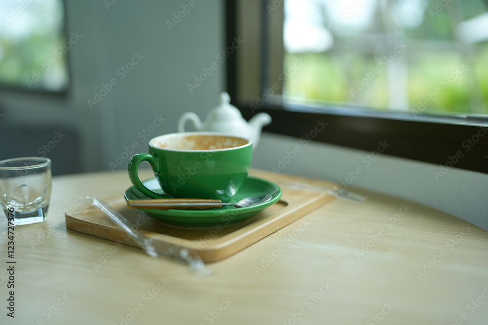 Empty green cup after drink coffee on a wooden table near window. The concept for ending break or something else. Empty green cup after drink coffee on a wooden table near window. The concept for ending break or something else.