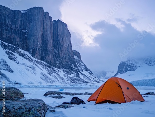 Orange tent nestled amidst snow covered rocks and majestic mountains under cloudy sky
