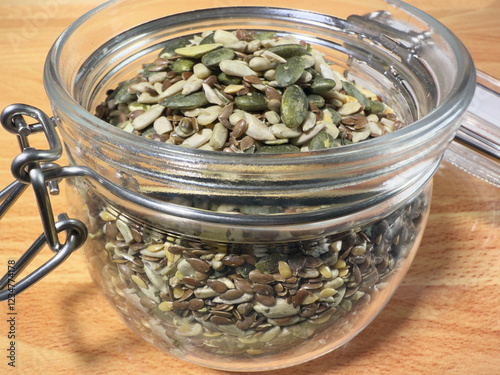 Macro closeup of mixed edible seeds (sunflower, pumpkin, hemp and linseed) in a nearly full, open glass storage jar. 