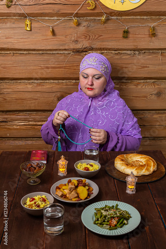 Muslim woman in purple hijab reads dhikr with rosary in hands at festive table Eid al-Fitr photo