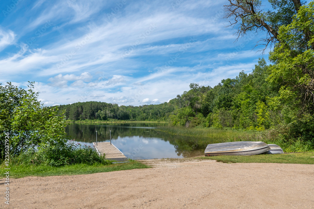 Beautiful Minnesota lake at a public boat launching site with a dock and a couple boats on the shore.