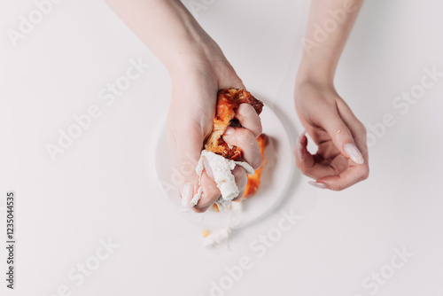 Woman's hands tearing, unwrapping, and crushing a pastry on a white plate against a white background