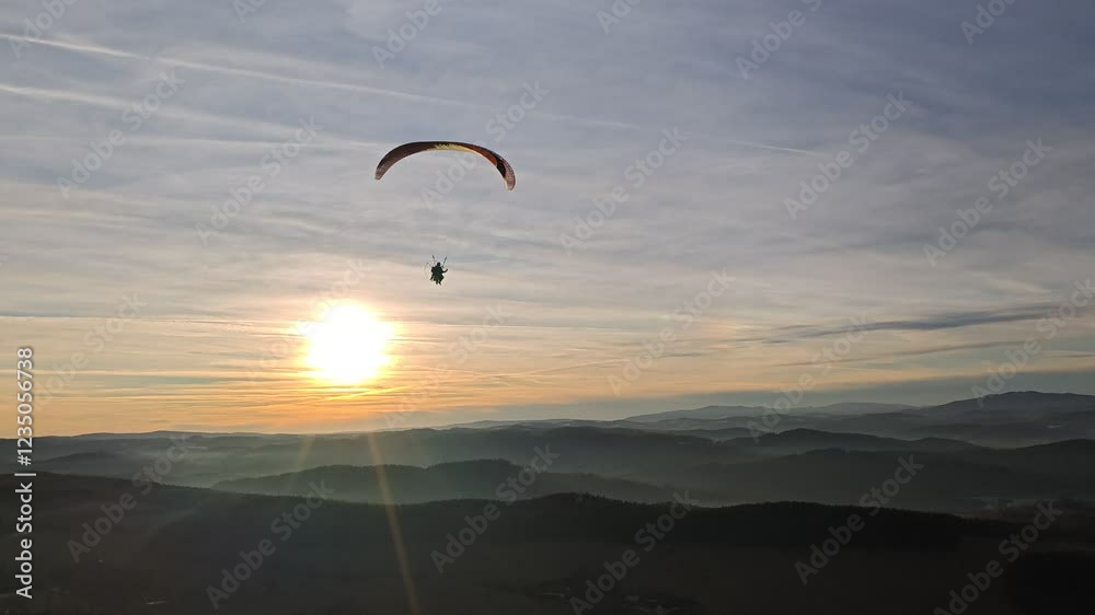 Aerial view of powered paraglider flying over mountainous landscape and forests, concept of adventure sports and aerial freedom-paragliding Aerial view of powered paraglider flying over mountainous landscape and forests, concept of adventure sports and aerial freedom-paragliding
