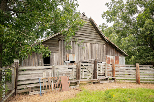A weathered wooden barn with a rustic fence in a lush rural setting