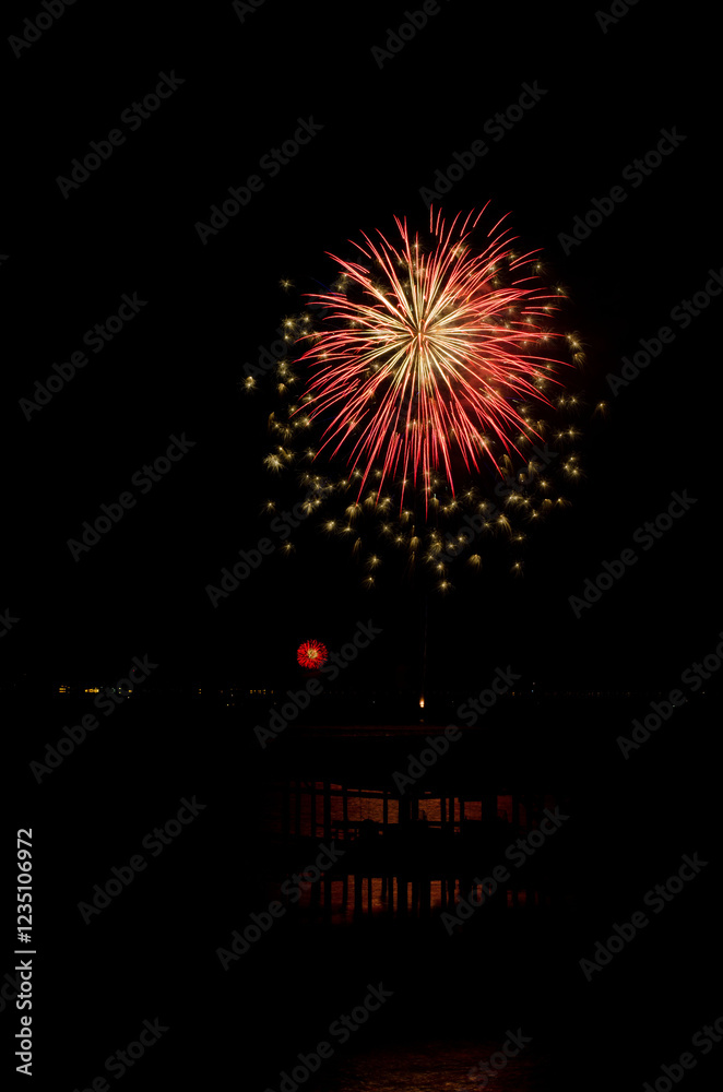 Red and gold fireworks explode in the night sky over a waterfront Red and gold fireworks explode in the night sky over a waterfront