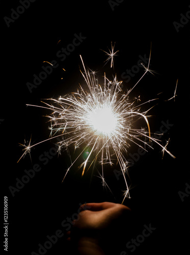 A bright sparkler glows in the dark, held by a person's hand