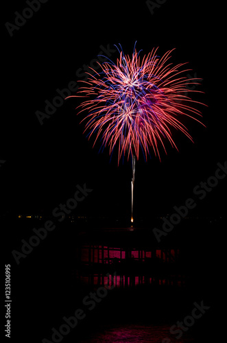 Red and blue fireworks explode over a waterfront with reflections photo