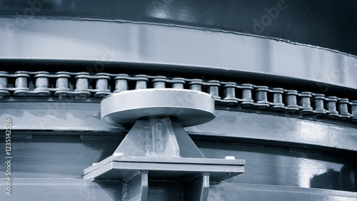 A metal chain is connected to a metal plate. The chain is visible from the side, and it is quite long. The plate is also made of metal