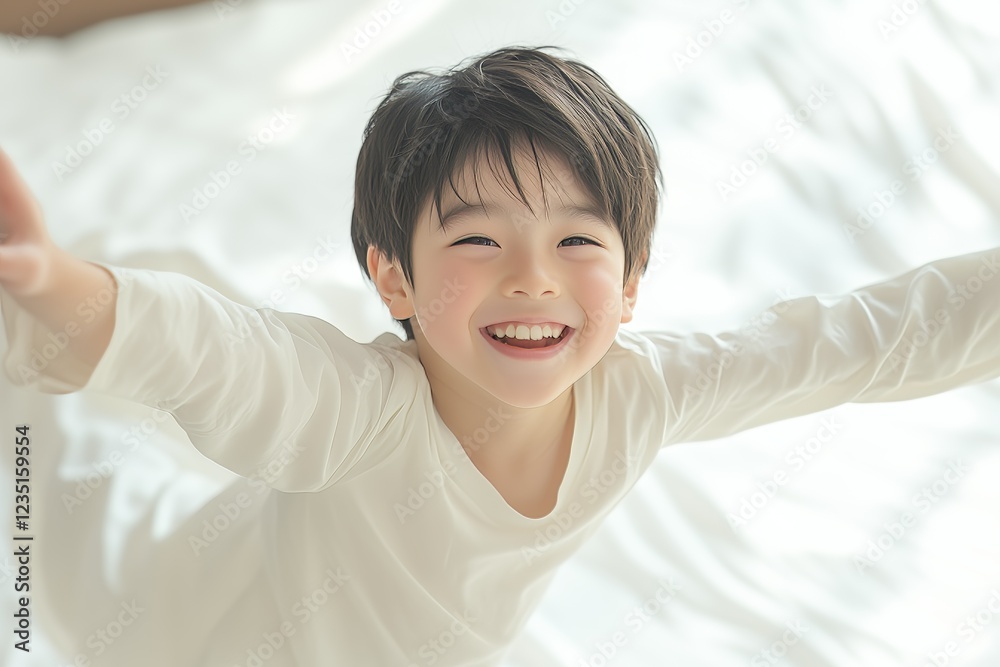 A cheerful child in a white outfit exudes happiness while playfully posing with outstretched arms on a soft bed. A cheerful child in a white outfit exudes happiness while playfully posing with outstretched arms on a soft bed.