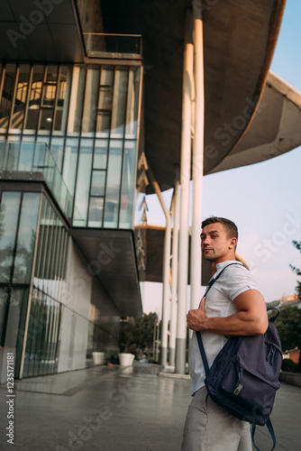 A man in a white shirt standing in front of a modern architectural building with glass and curved structures photo