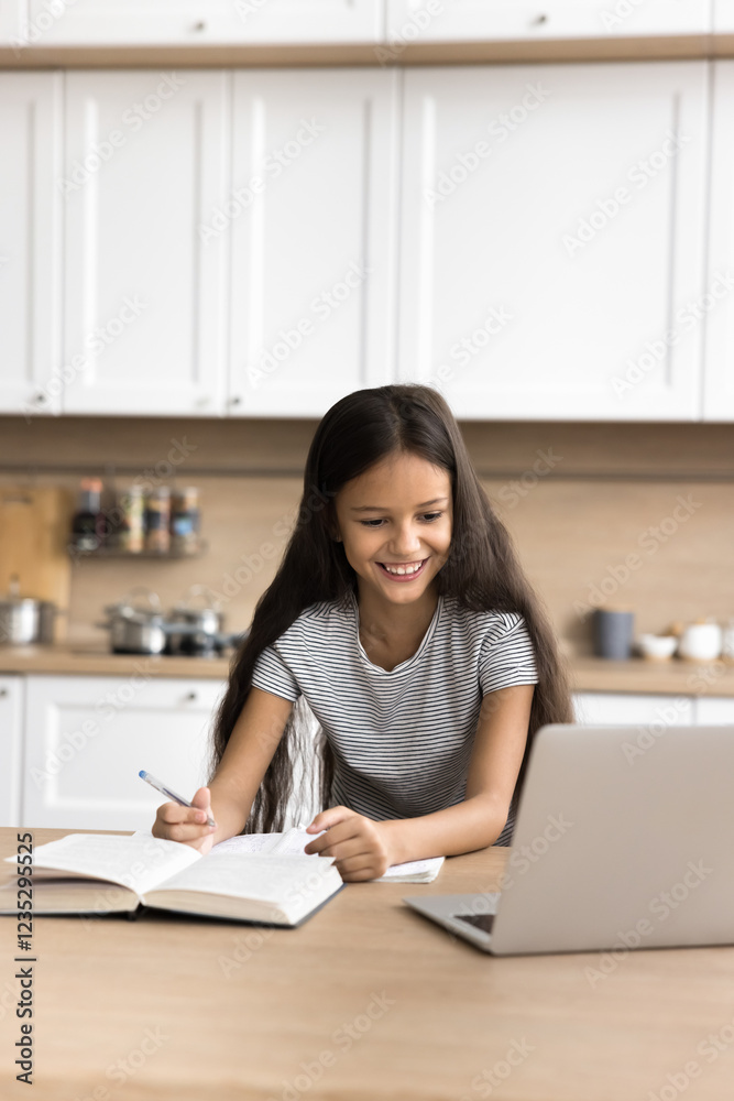 E-learning. Attentive little pupil junior school age girl use pc to study at home kitchen listen to teacher giving distant lesson on classroom platform do written task take brief notes. Vertical photo E-learning. Attentive little pupil junior school age girl use pc to study at home kitchen listen to teacher giving distant lesson on classroom platform do written task take brief notes. Vertical photo