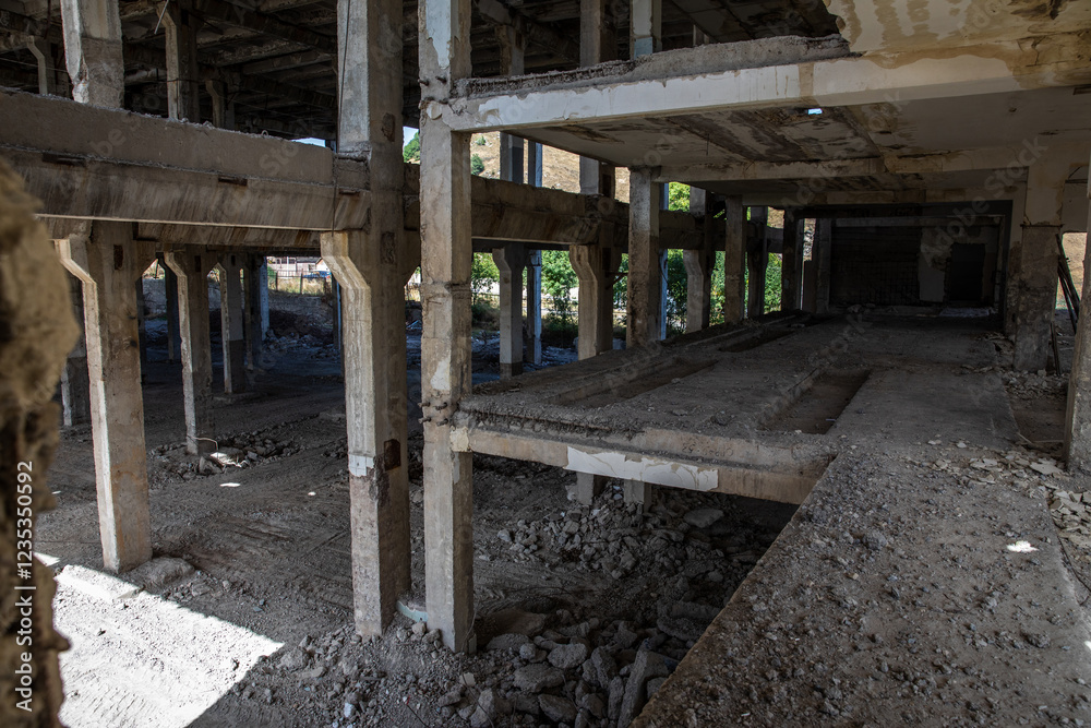 An unfinished building reveals exposed concrete pillars and debris in a construction site.
Sunlight illuminates the open spaces between the concrete supports of an abandoned structure.