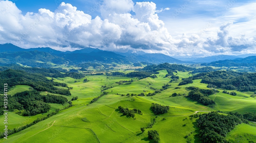 Obraz premium Aerial view of rolling green hills, mountains, and blue sky
