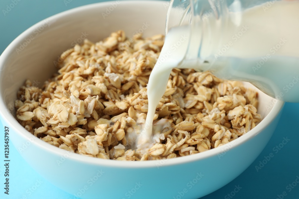 Pouring milk into bowl with oatmeal at light blue table, closeup Pouring milk into bowl with oatmeal at light blue table, closeup