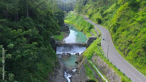 Road by a flowing river, in the middle of forests and hills with lush trees in Sempor Kebumen Central Java photo