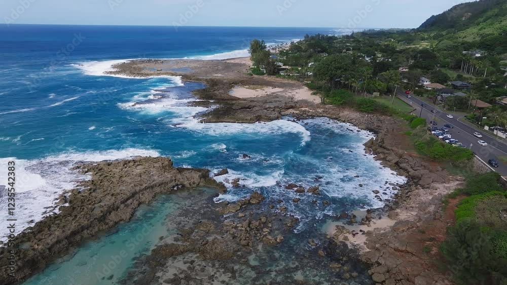 Aerial view of a rocky coastline on Oahu island, Hawaii, with waves crashing, a small beach, lush greenery, and a residential area with a coastal road. Aerial view of a rocky coastline on Oahu island, Hawaii, with waves crashing, a small beach, lush greenery, and a residential area with a coastal road.
