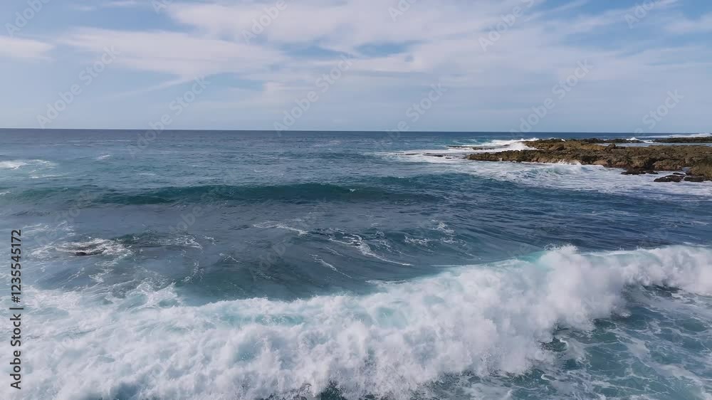 Serene aerial view of turquoise waves rolling and breaking on Oahu's rocky coast, with white foam and a partly cloudy sky on the horizon. Serene aerial view of turquoise waves rolling and breaking on Oahu's rocky coast, with white foam and a partly cloudy sky on the horizon.