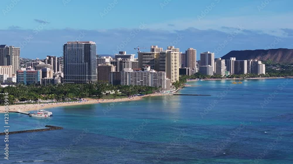 A slow pan of Waikiki Beach in Oahu, Hawaii, with Diamond Head crater, turquoise waters, surfers, boats, and Honolulu's skyline along the coast. A slow pan of Waikiki Beach in Oahu, Hawaii, with Diamond Head crater, turquoise waters, surfers, boats, and Honolulu's skyline along the coast.