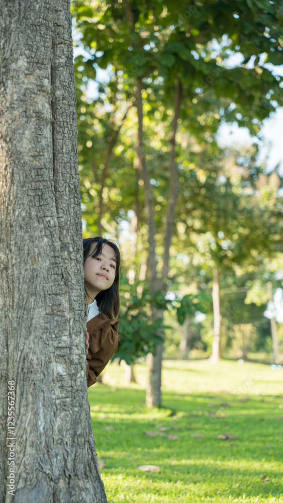 Child girl peeking out from behind the tree in green park Child girl peeking out from behind the tree in green park