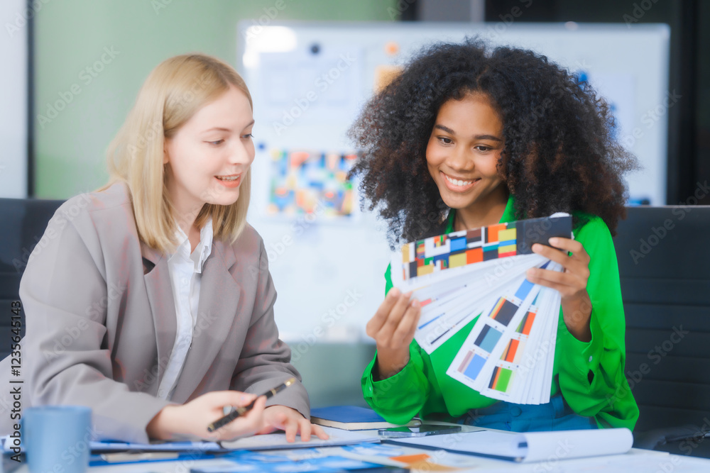 Fototapeta premium A young African American woman and a young Russian woman work together in a business office. They discuss UX design, using color swatches and tablets, while planning layouts and interfaces.