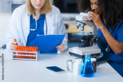 Young African American and Russian woman, both scientists, collaborate to analyze blood samples, viruses, vaccines using microscopes. They conduct crucial medical and biological research. photo