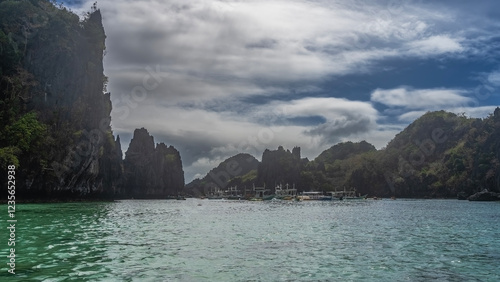 The emerald lagoon is surrounded by steep karst cliffs. Traditional Filipino bangka boats are anchored in the bay. Blue sky, clouds. Philippines. Palawan. Small lagoon. Bacuit Bay. photo