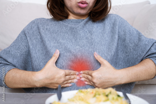 Asian woman suffering from epigastric burning and pain due to dyspepsia and acid reflux, feeling discomfort in upper abdomen after eating food