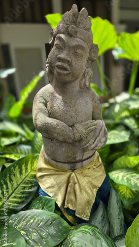 Garden Gnome traditional stone statue situated in a tranquil tropical garden, surrounded by vibrant foliage and artistic decor, harmonizing with the natural beauty of its environment