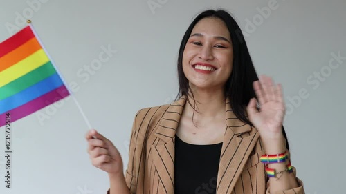 Happy smiling non-binary LGBT person saying hi, waiving welcoming hand, showing rainbow flag for LGBT awareness pride month