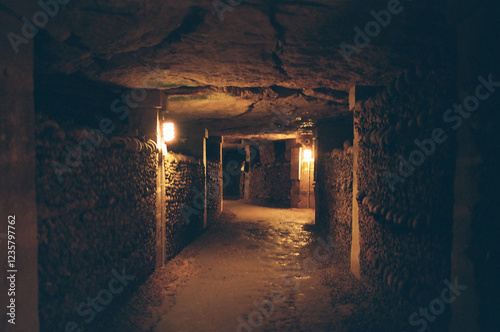 Photography Dimly lit underground tunnel lined with human bones and skulls.