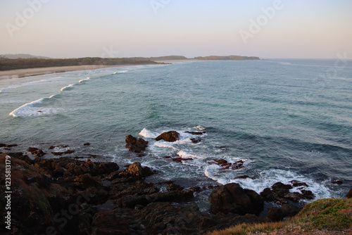  A panoramic view of a coastal landscape with sandy beach, crashing waves, and rocky shoreline 
