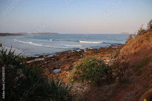 Coastal landscape with rocky shore, ocean waves, and distant islands