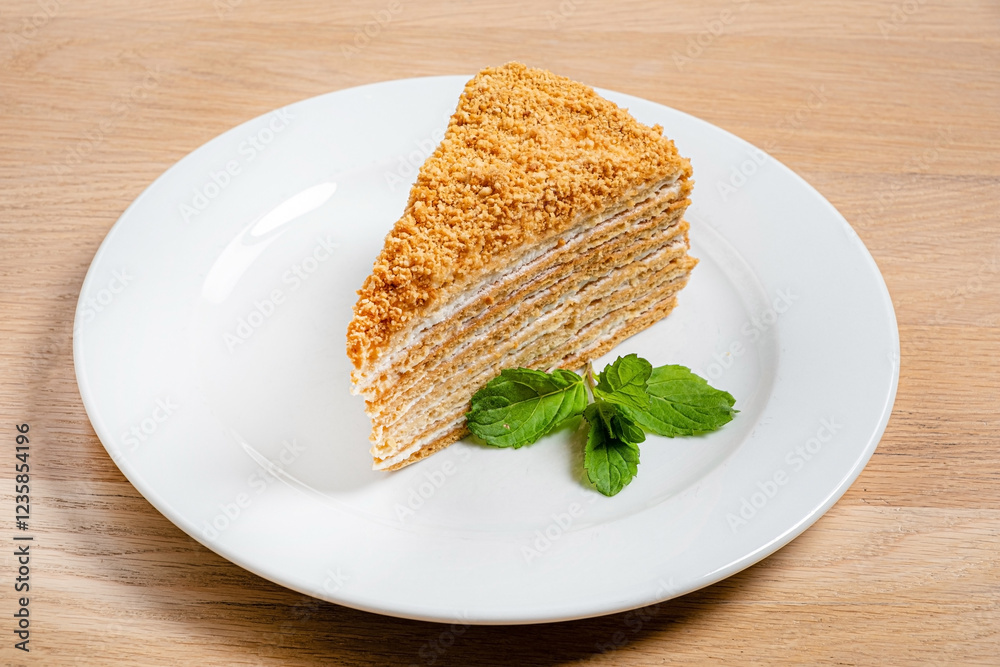 A luscious slice of honey cake is presented elegantly on a white plate, adorned with vibrant mint leaves. The cake’s layered texture invites indulgence and delight. A luscious slice of honey cake is presented elegantly on a white plate, adorned with vibrant mint leaves. The cake’s layered texture invites indulgence and delight.