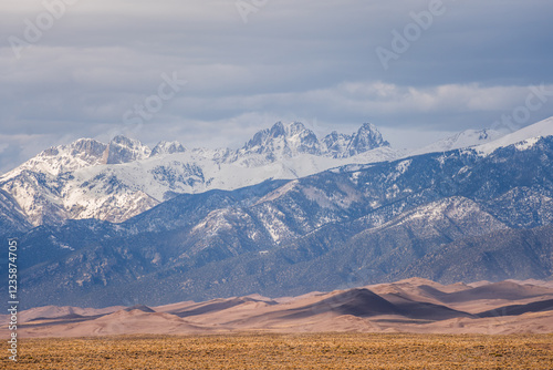 Sand dunes at the base of snow capped mountain peaks photo